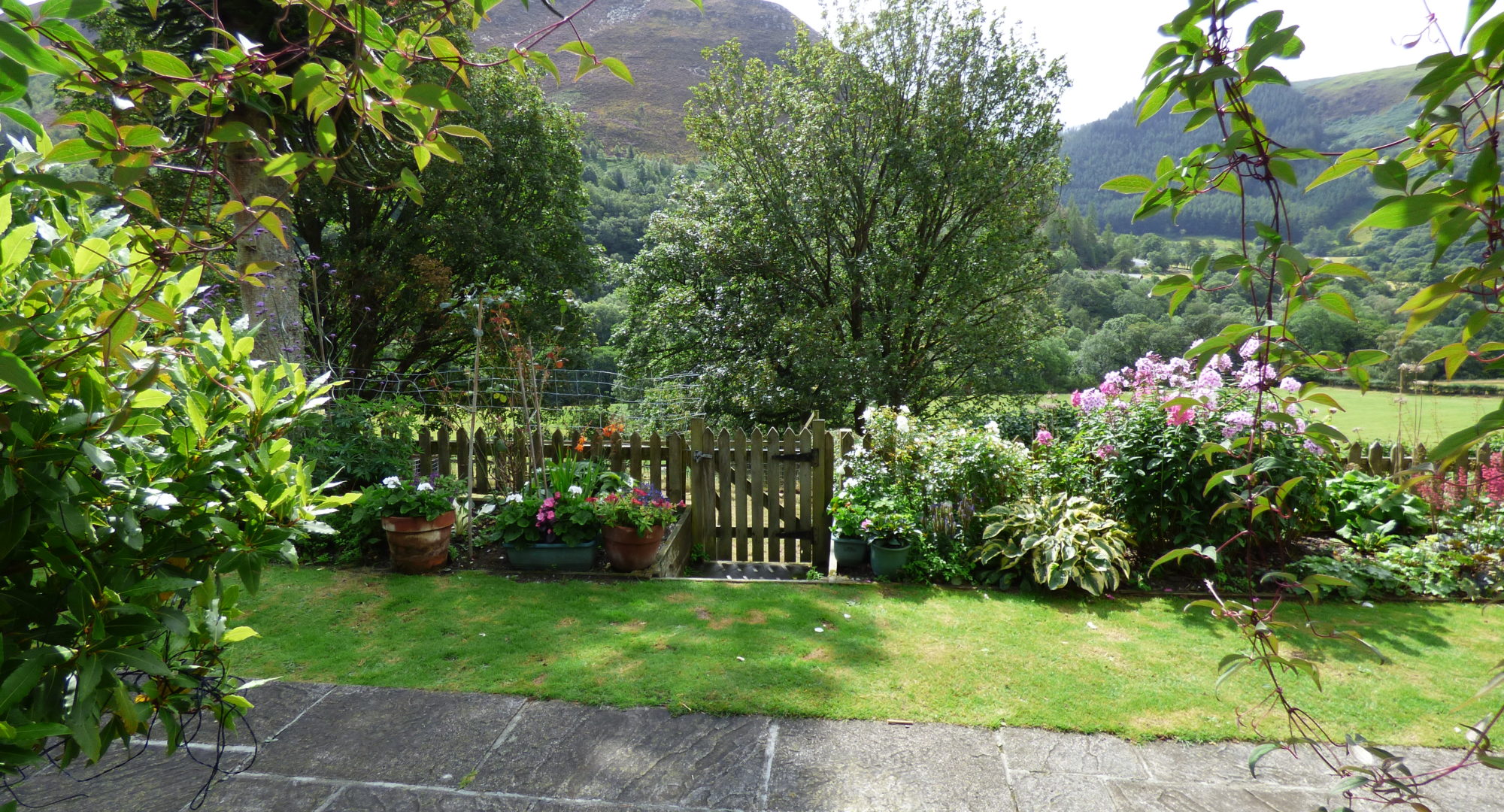 The back garden of a cottage with a hot tub, with flowers and picket fence